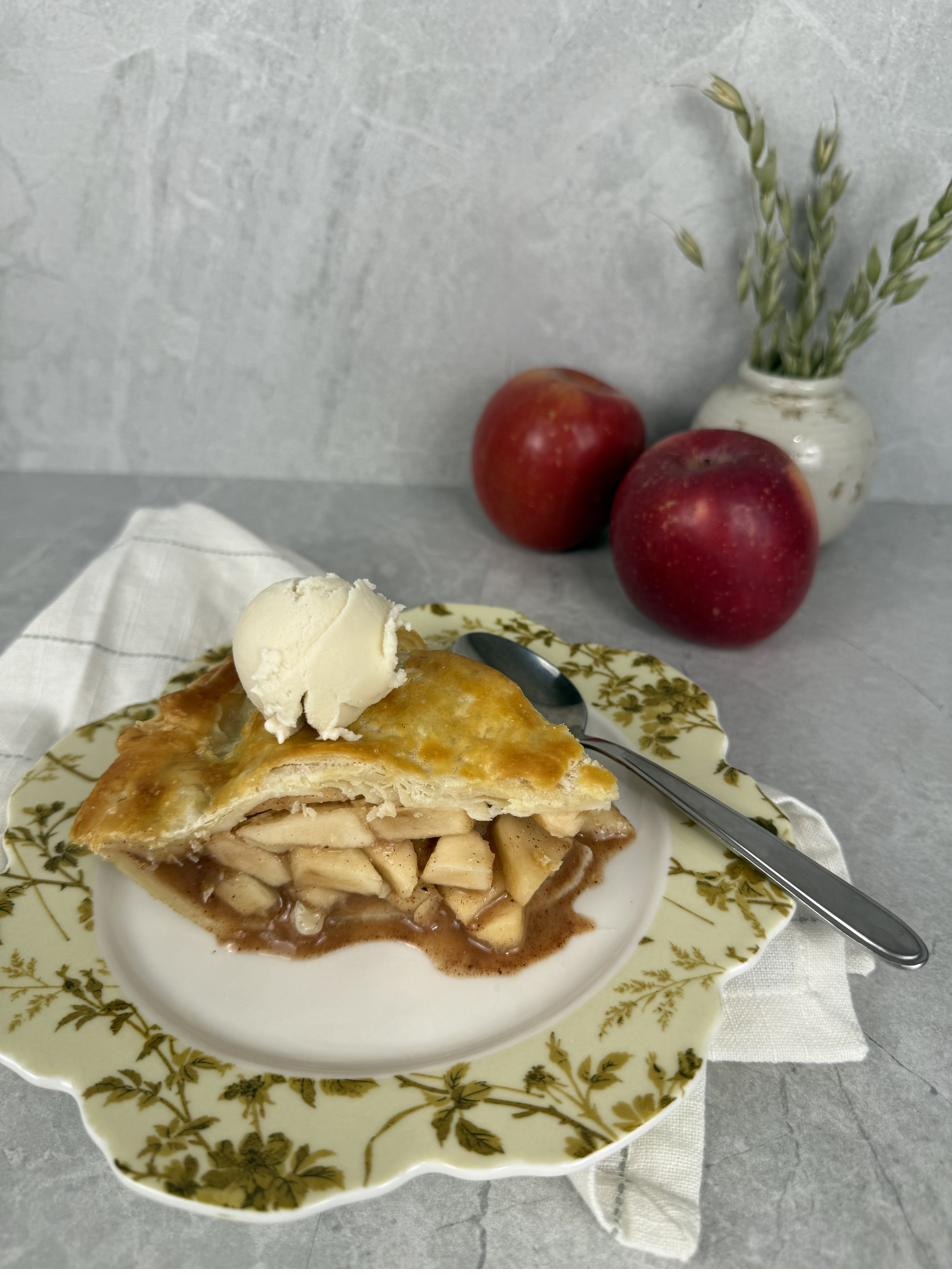 A warm slice of apple pie with a scoop of ice cream melting alongside