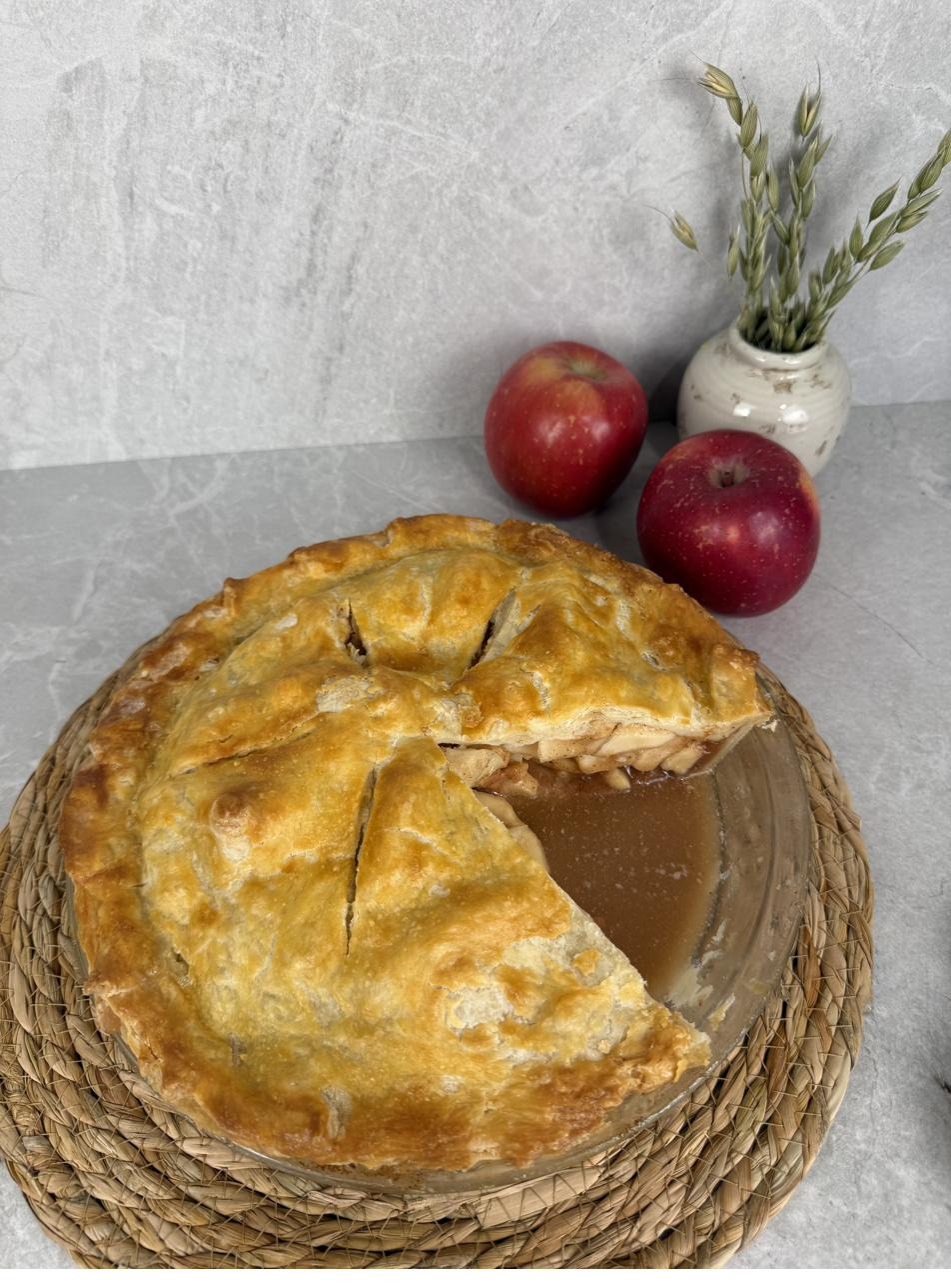 A golden New England apple pie cooling, with red apples and rosemary
