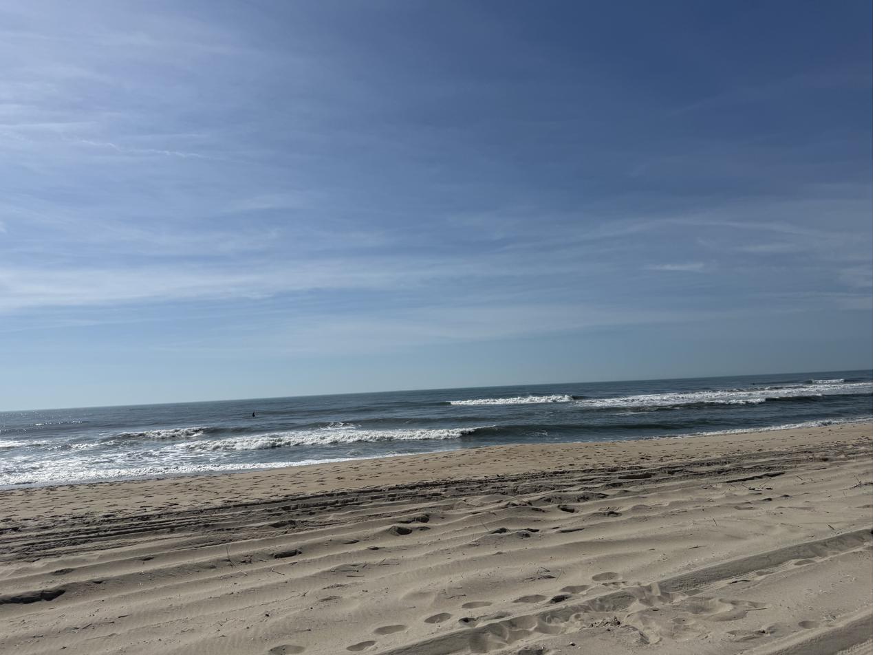 A wide, empty stretch of beach with footprints in the sand under a hard blue sky