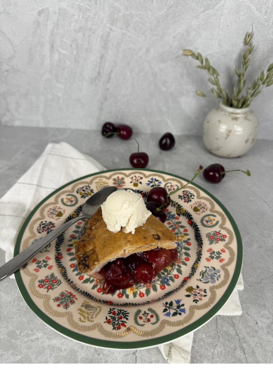 A slice of cherry pie served with a scoop of ice cream