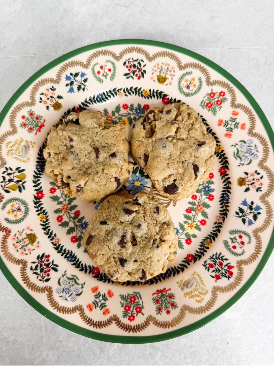 Three chocolate chip cookies on a floral-rimmed plate, seen from above