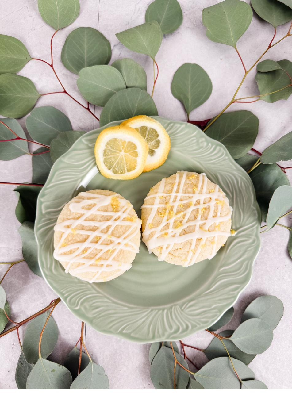 Lemon sugar cookies with lemon slices on a green plate surrounded by eucalyptus
