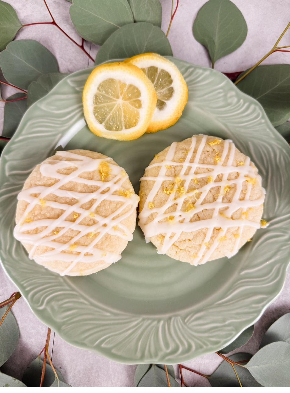 Two glazed lemon sugar cookies on a green scalloped plate with lemon slices