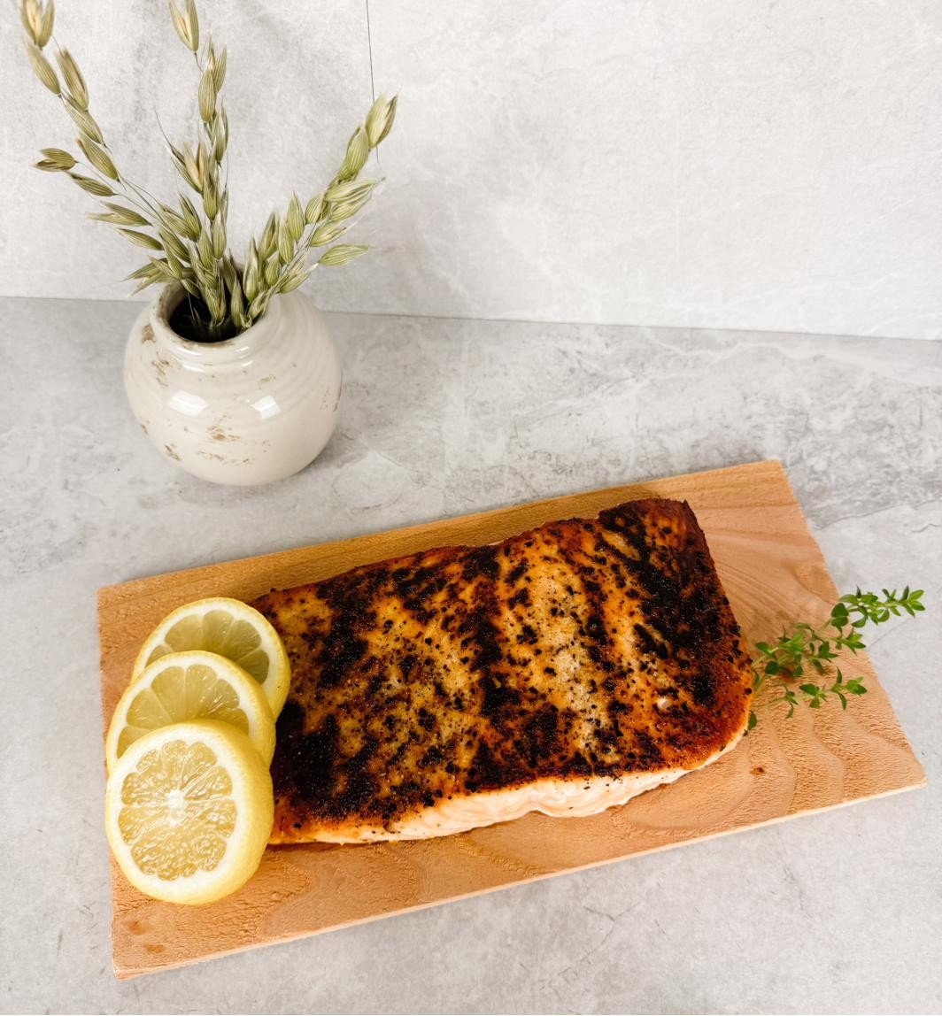 A pan-seared salmon fillet on a wooden board with lemon slices and thyme