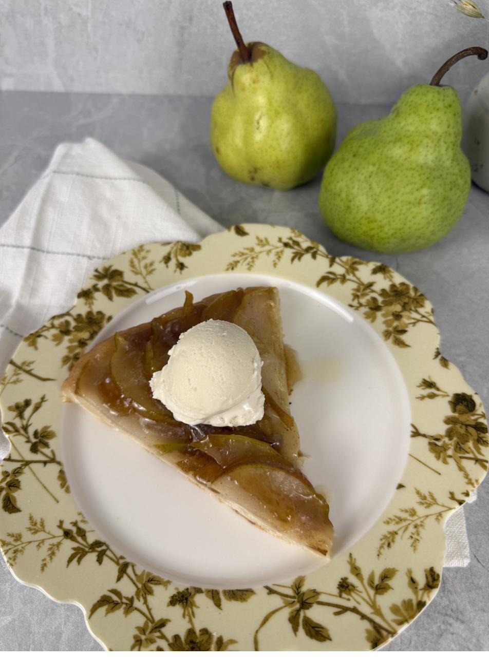 A slice of pear tarte tatin with a scoop of ice cream and fresh pears alongside