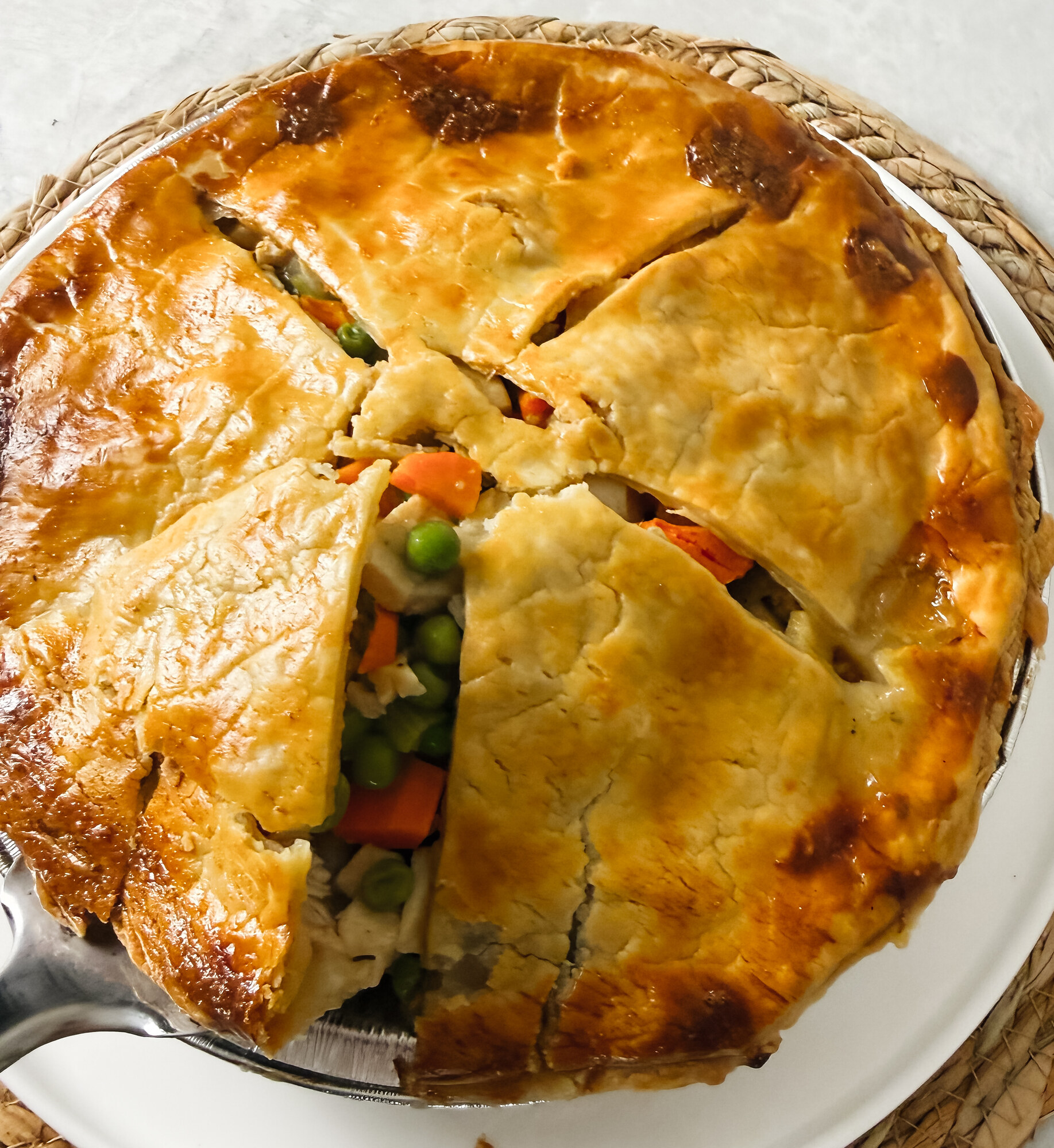 A wedge of turkey potpie lifted on a white plate, showing peas, carrots, and turkey in a creamy filling