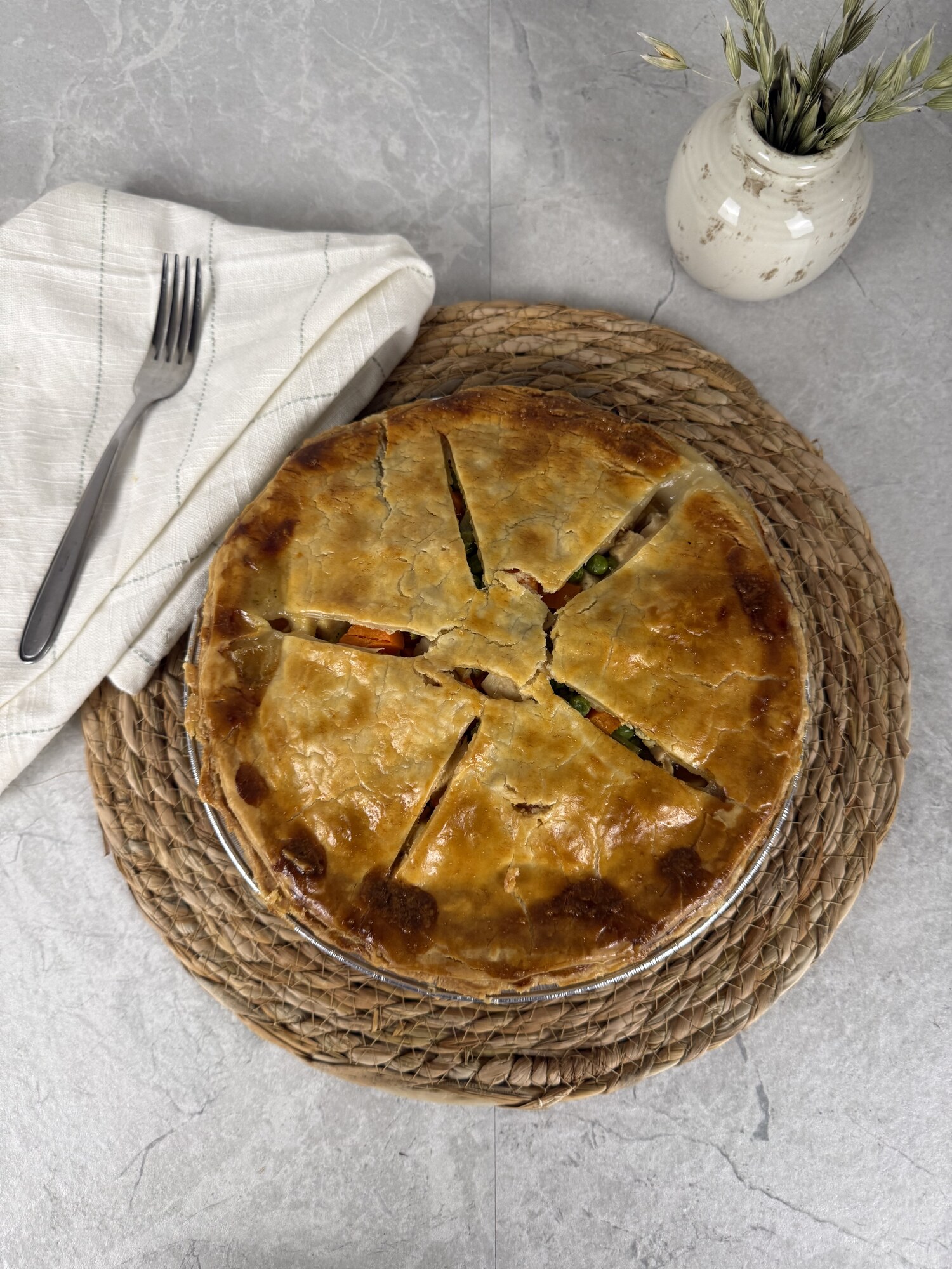 An overhead view of a golden turkey potpie on a woven mat with a linen napkin and fork